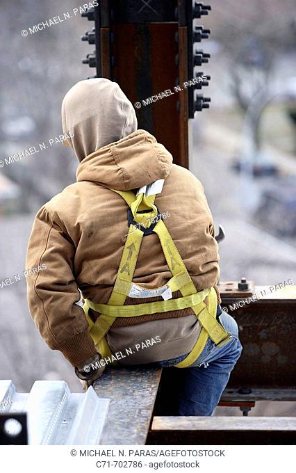 Iron/construction worker from back with safety harness on sitting on steel beam