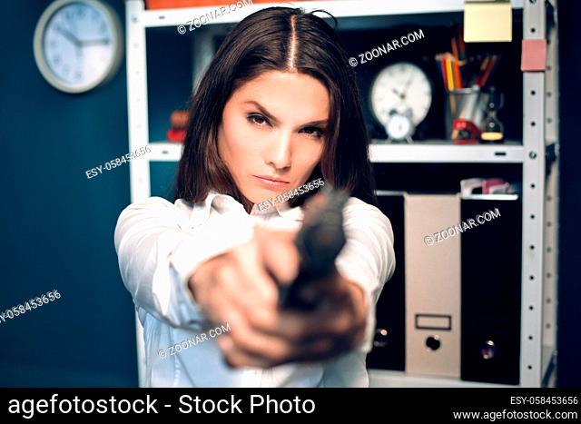 Business lady holding gun with both of her hands. Angry business woman wearing white blouse pointing gun straight to camera with serious look on her face
