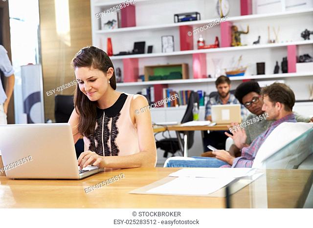 Businesswoman Working On Laptop In Busy Office