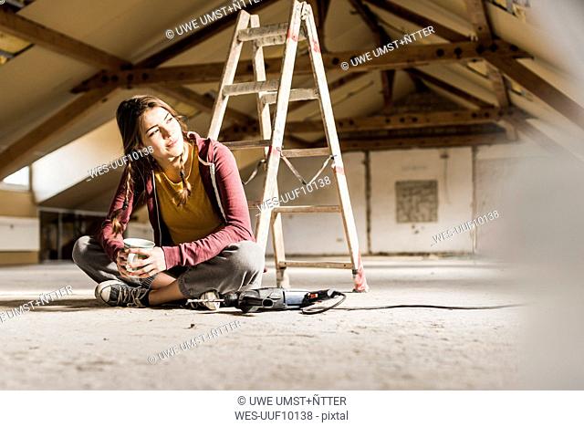 Independent young woman renovating her new home, sittiing on floor with cup of coffee