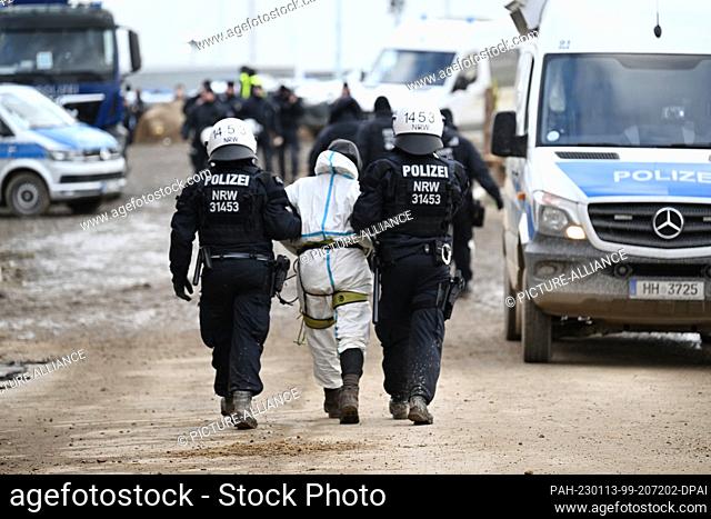 13 January 2023, North Rhine-Westphalia, Erkelenz: An activist is escorted from the site on the third day of the eviction in the lignite hamlet of Lützerath...
