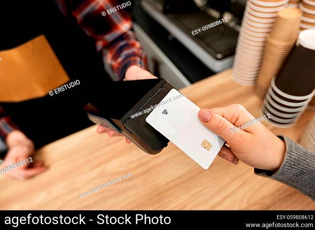close-up, customer hand holding credit card near nfc terminal. barista accepts payment from credit card via pos machine in coffee shop