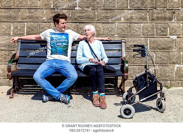 An Elderly Disabled Woman Sitting On A Bench Talking To Her Grandson, Brighton, Sussex, UK