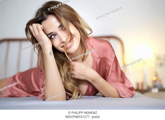 Smiling young woman in dressing gown lying in bed looking sideways