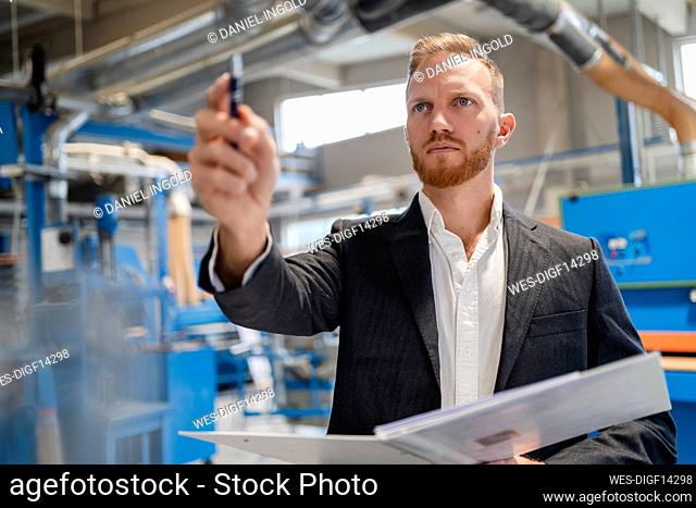 Portrait of¶ÿwell-dressed¶ÿcarpenter standing in production hall with ring binder in hands
