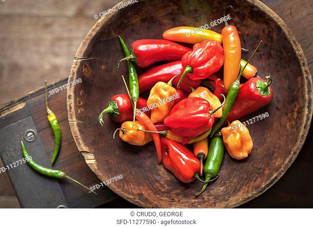 Various chilli peppers and peppers in a wooden bowl