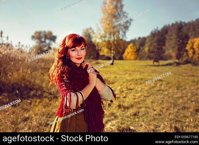 Beautiful young woman in long skirt and red wool scarf standing outdoors in countryside. Outdoor shot. Natural background. Copy space