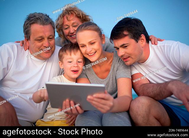 Happy big family having good time together. Grandparents and parents looking at the pad screen while boy using it