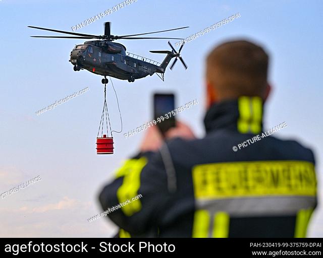 30 March 2023, Brandenburg, Müncheberg: A Sikorsky CH-53 helicopter of the German Air Force flies over Müncheberg-Eggersdorf airfield with a water tank during...