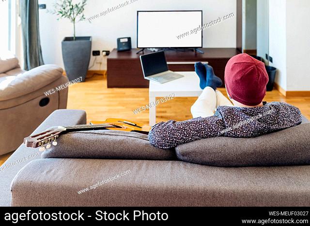 Male guitarist watching TV on sofa at home