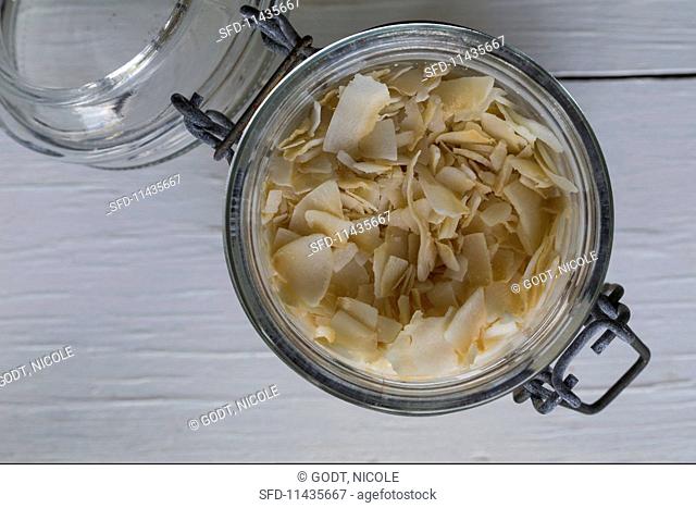 Coconut chips in a flip-top jar on a white wooden surface