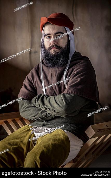 Middle Ages - second half of 14th Century. Hypothetical reenactment of Northern Italy customs and traditions. Portrait of a young man with beard and hat sitting...
