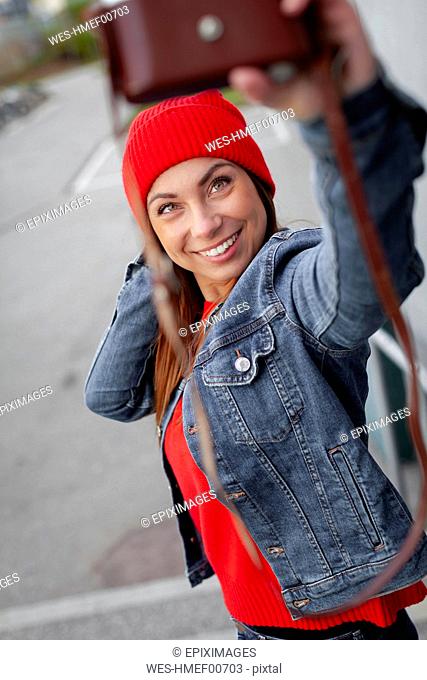 Woman wearing red pullover, jeans jacket and wolly hat and taking a selfie