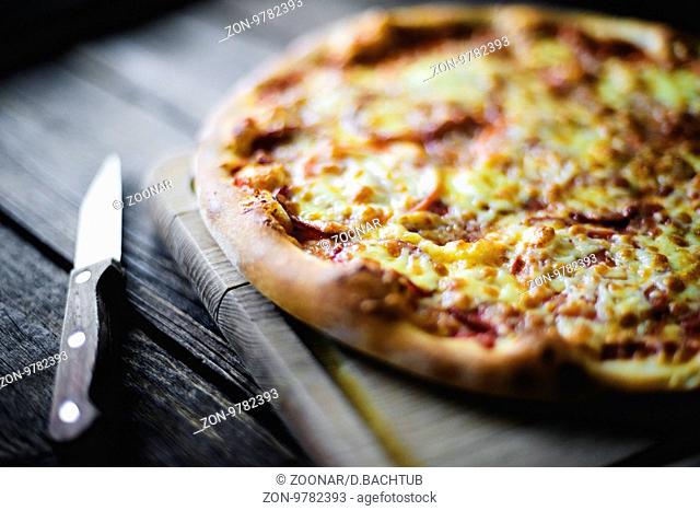 pizza with sausage and cheese on a cutting board and knife beside