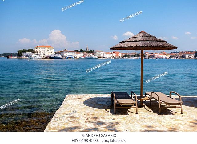 Histroric Istrian town of Porec, Croatia as seen from the sea and Sveti Nikola island, beach with chairs and parasol in front