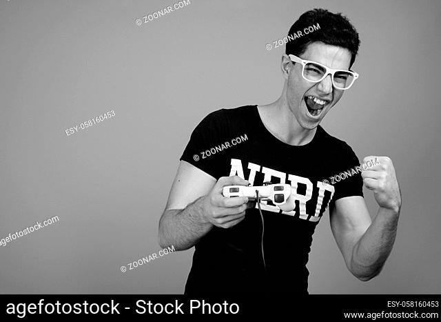 Studio shot of young handsome Persian nerd man with eyeglasses against gray background in black and white