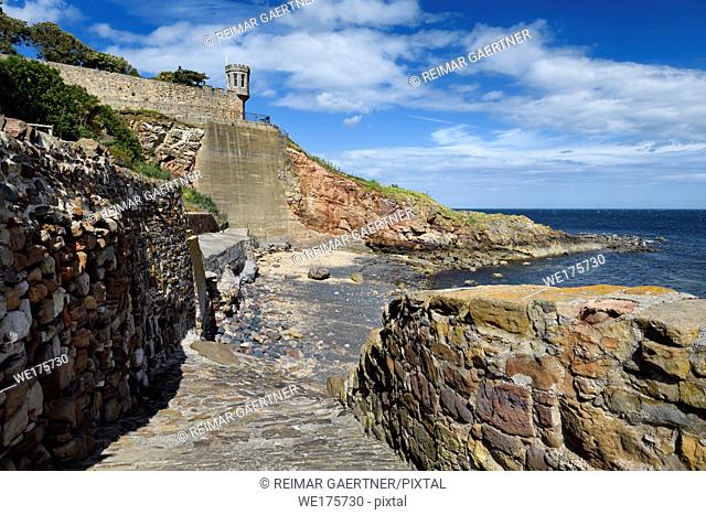 Rock wall path to beach at Crail in Fife Scotland UK with lookout tower turret of Crail House over the North Sea