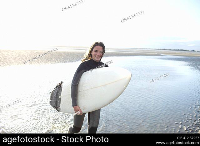 Portrait happy young female surfer with surfboard in sunny ocean surf