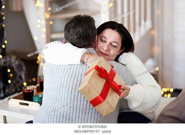 Happy mature couple with gift box hugging in living room