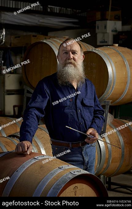 Vintner standing beside wooden wine barrels