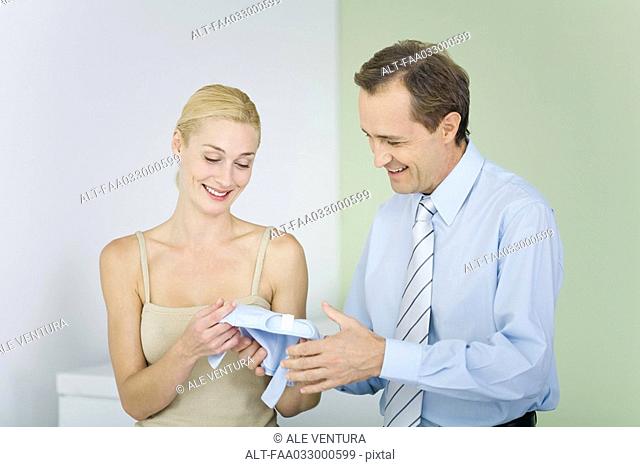 Couple looking at baby clothing together, both smiling