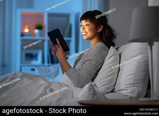 asian woman with tablet pc in bed at home at night