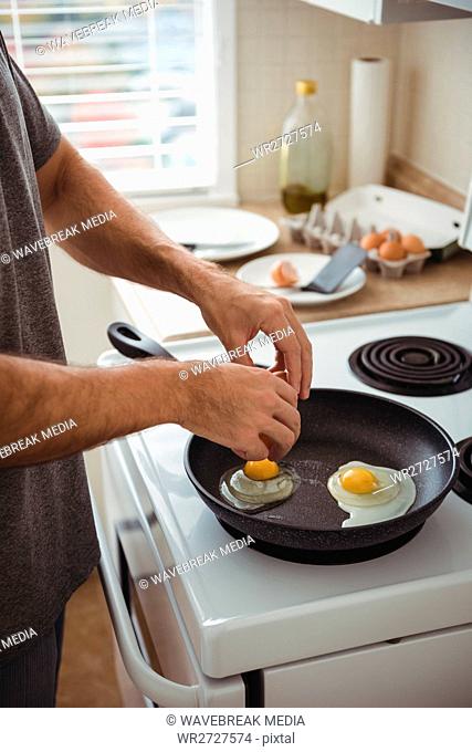 Man cracking an egg into a frying pan in the kitchen