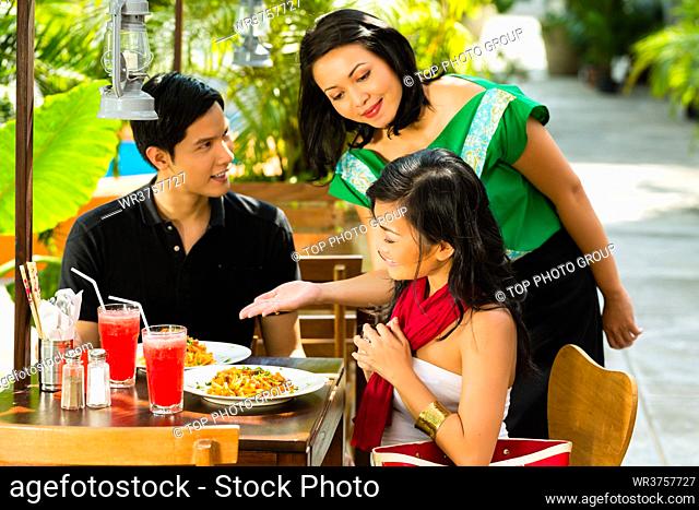 Asian man and woman in restaurant are being served food by the waitress