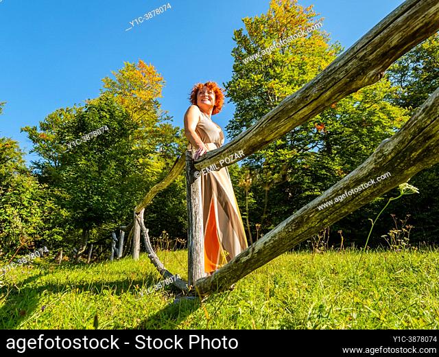 Mature woman in countryside is standing behind a wooden fence laughing looking back