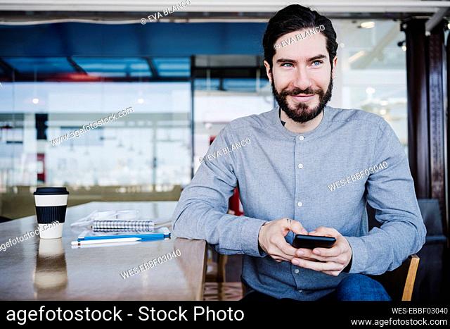 Smiling creative person holding mobile phone while looking away at work place