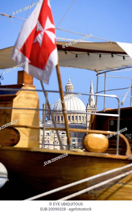 The dome of the Carmelite Church of 1573 seen through the foredeck of an old schooner with a Maltese Cross flag moored on Sliema waterfront