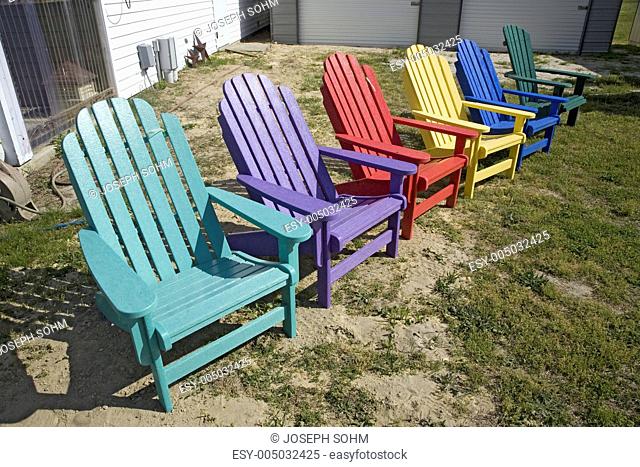 Rainbow colored wooden chairs, known as Maine Chairs, standing in a row outside on the Eastern Shore, Maryland