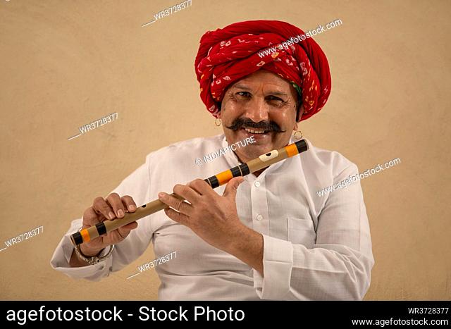 PORTRAIT OF A TURBANED MAN HAPPILY HOLDING FLUTE IN HIS HAND