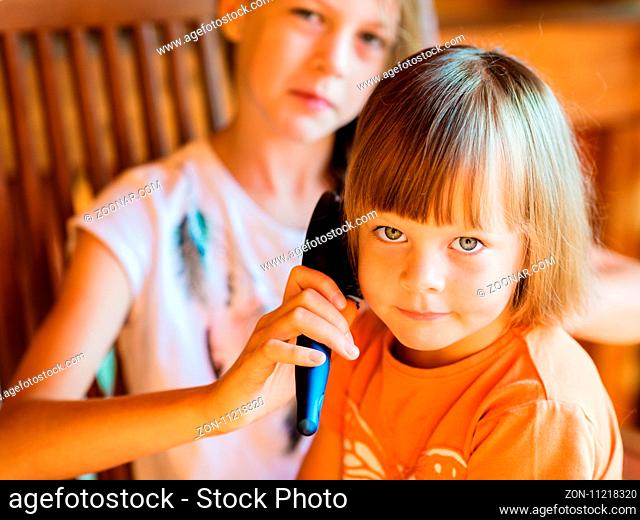 Charming little girl is looking at camera and smiling while her beautiful older sister is combing her hair
