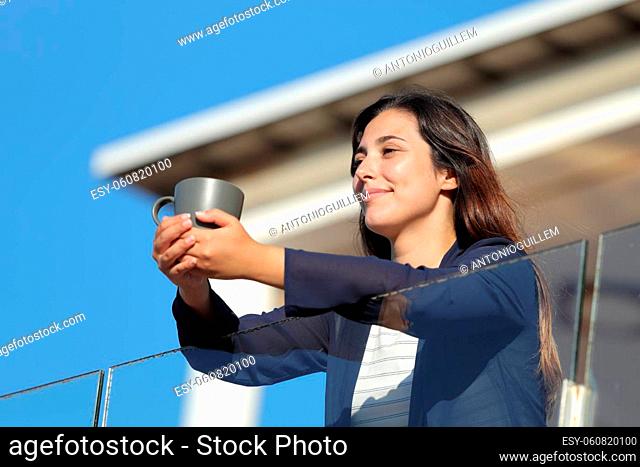 Woman holding coffee cup relaxing contemplating views in an apartment balcony a sunny day