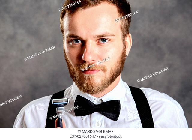 young bearded man in white shirt and bow tie showing shaver