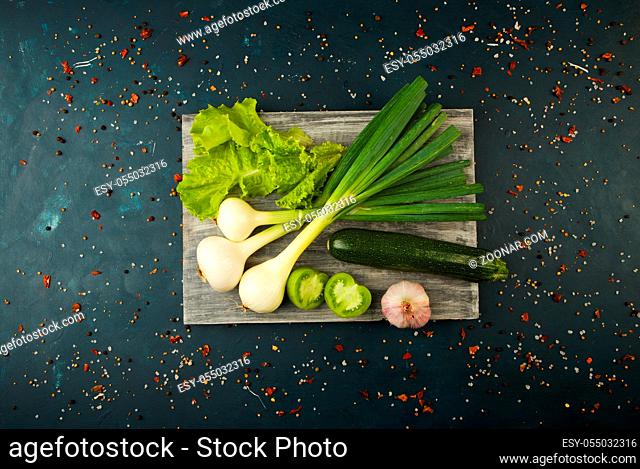FRESH VEGETABLES AND SPICES ON A WOODEN BOARD ON A DARK STONE BACKGROUND. THE CONCEPT OF VINTAGE. SPICES THE YOUNG CORN ASPARAGUS GREEN TOMATO CUCUMBER ON A...