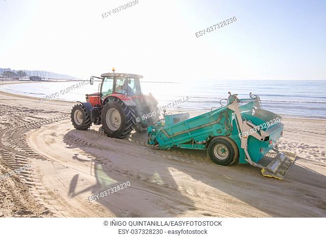 red tractor with green trailer cleaner cleaning sand in Els Terrers Beach, Benicassim, Castellon, Valencia, Spain, Europe. Mediterranean Sea