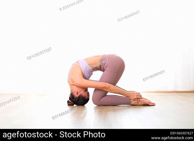 Portrait of gorgeous active sporty young woman practicing yoga in studio. Beautiful girl practice Sasangasana, rabbit yoga pose