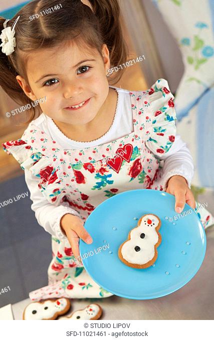 A little girl holding a gingerbread snowman on a plate