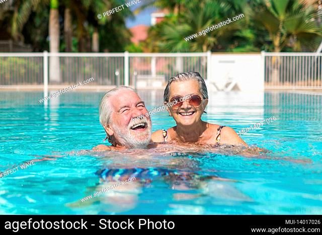 couple of two happy seniors having fun and enjoying together in the swimming pool smiling and playing. happy people enjoying summer outdoor in the water