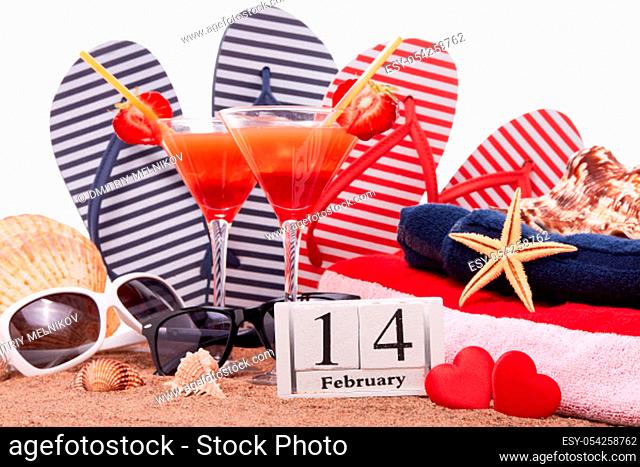Beach accessories, seashells, sand, two glasses with cocktail, red hearts and calendar with date 14 february on white background