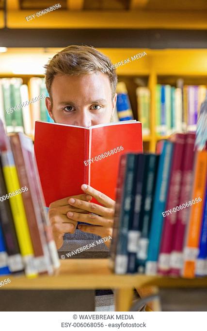 Male student holding book in front of his face in the library