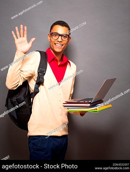 Handsome latin student in glasses with laptop computer waving to the camera in studio isolated on grey background