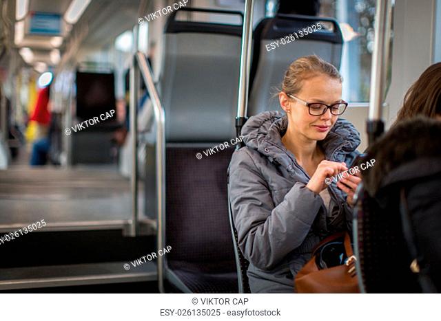 Pretty, young woman on a streetcar/tramway, during her commute to work. Using her smartphone. (color toned image; shallow DOF)