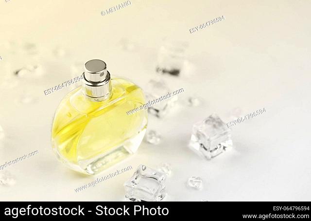 Female perfume yellow bottle, Objective photograph of perfume bottle in ice cubes and water on white table. View from above