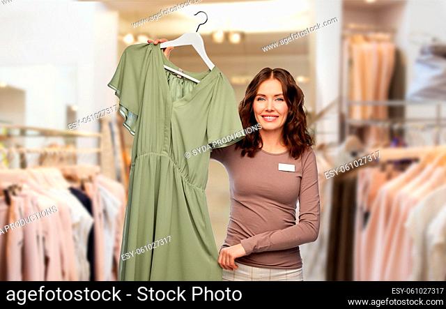 happy saleswoman with dress on hanger at shop