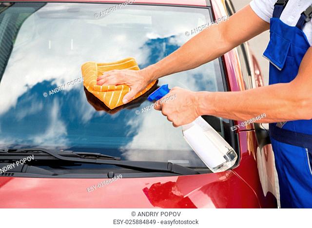 Mature male worker cleaning car windshield with cloth and spray bottle