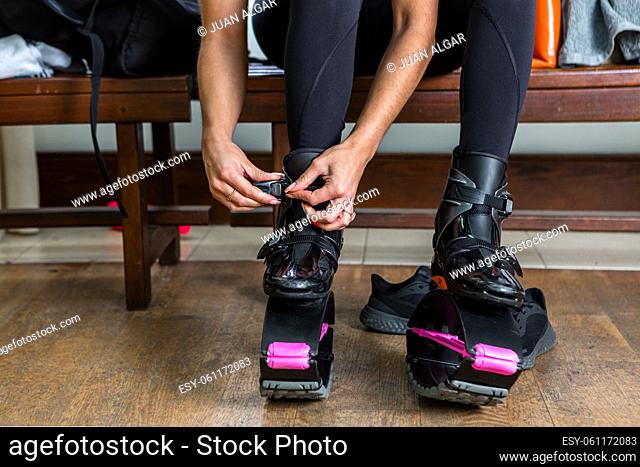 Unrecognizable female athlete fastening buckle on jumping shoes while sitting on bench in dressing room and preparing for fitness training in gym