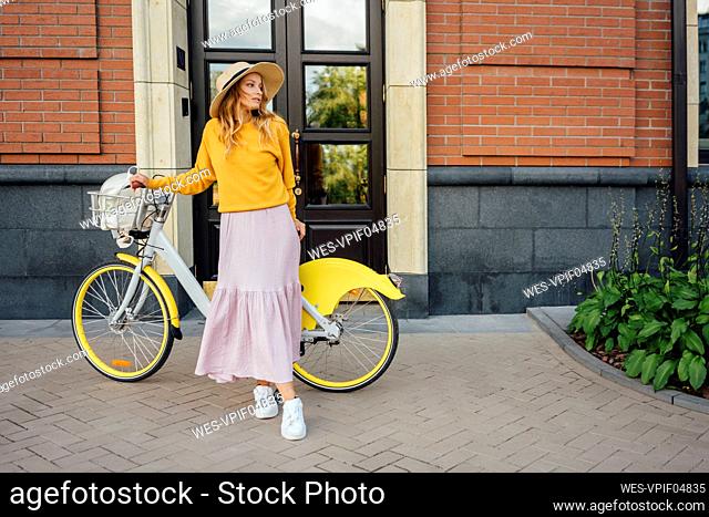 Young woman with bicycle standing in front of building